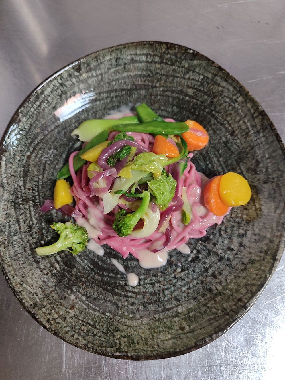 Nudelgericht mit rosa Nudeln, Gemüse und Sahnesauce auf einem grauen Teller.