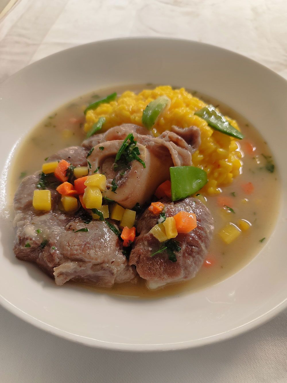 Ossobuco mit gelbem Risotto und Gemüse in einer weißen Schüssel.