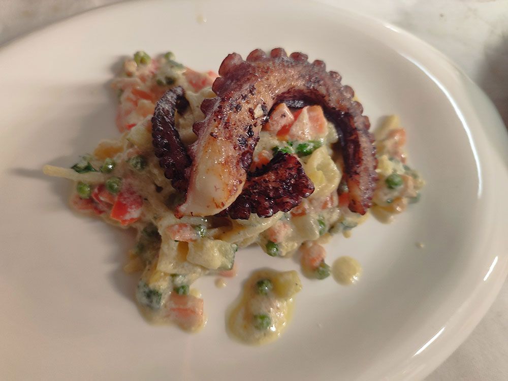 Gegrillte Oktopustentakel über einem cremigen Gemüsesalat auf einem weißen Teller.