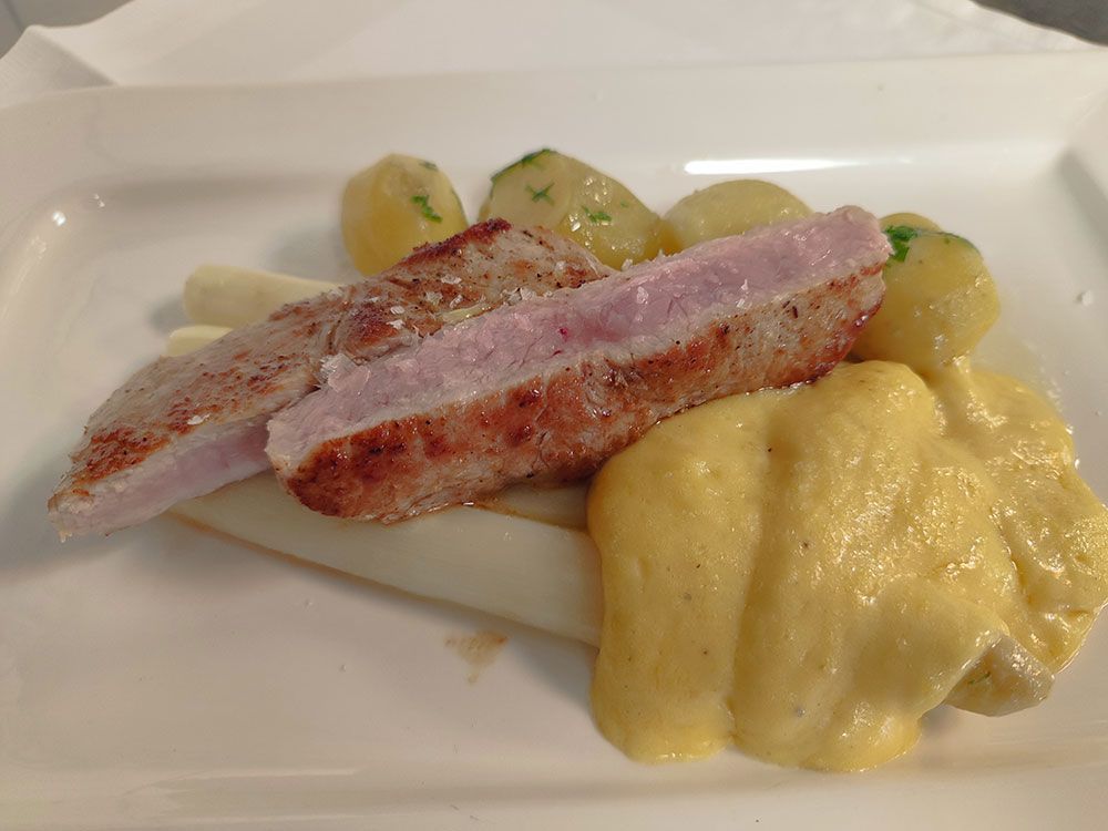 Geschnittenes Schweinefilet, Spargel, Kartoffeln und gelbe Soße auf einem weißen Teller.