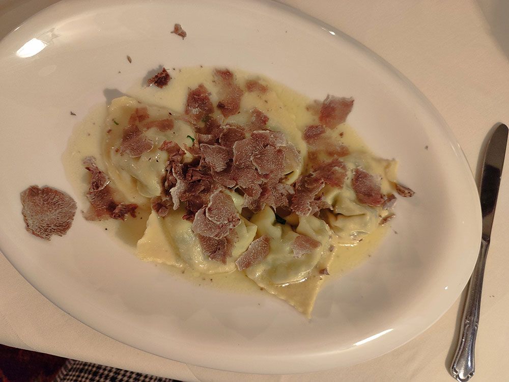 Pasta-Ravioli mit Trüffelraspeln und Sahnesauce auf einem weißen ovalen Teller.