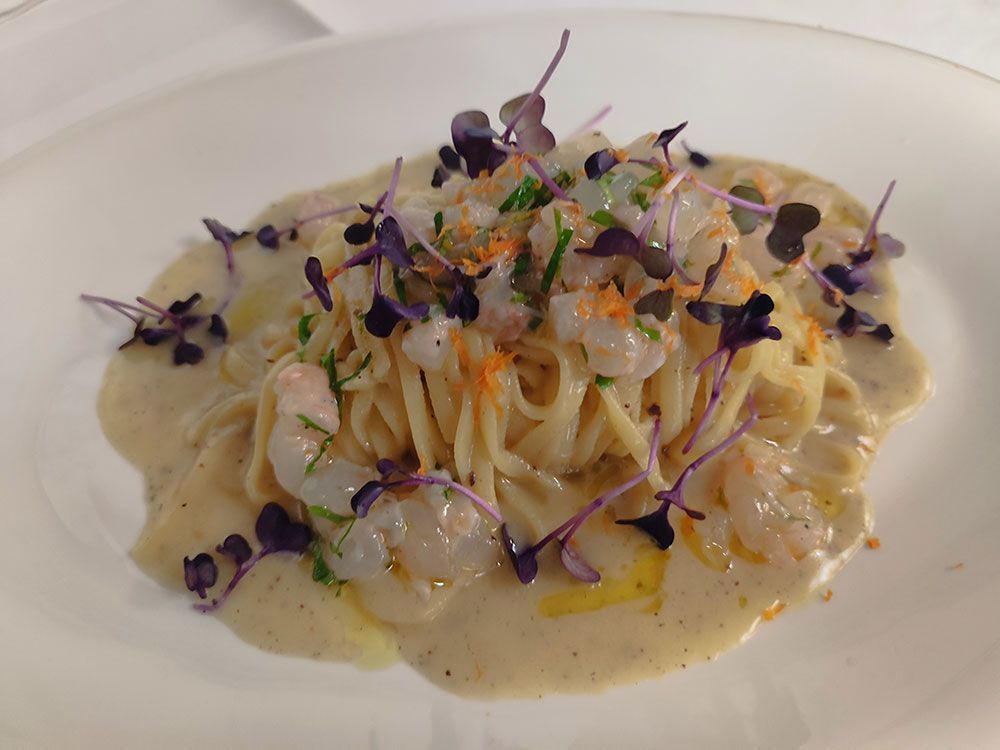 Nudelgericht mit Garnelen und Microgreens auf einem weißen Teller.