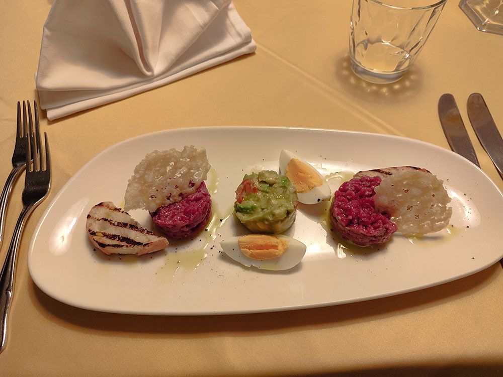 Teller mit bunten Vorspeisen: Rote Bete, Avocado, Ei und gegrilltes Obst, mit einer weißen Serviette und Besteck.