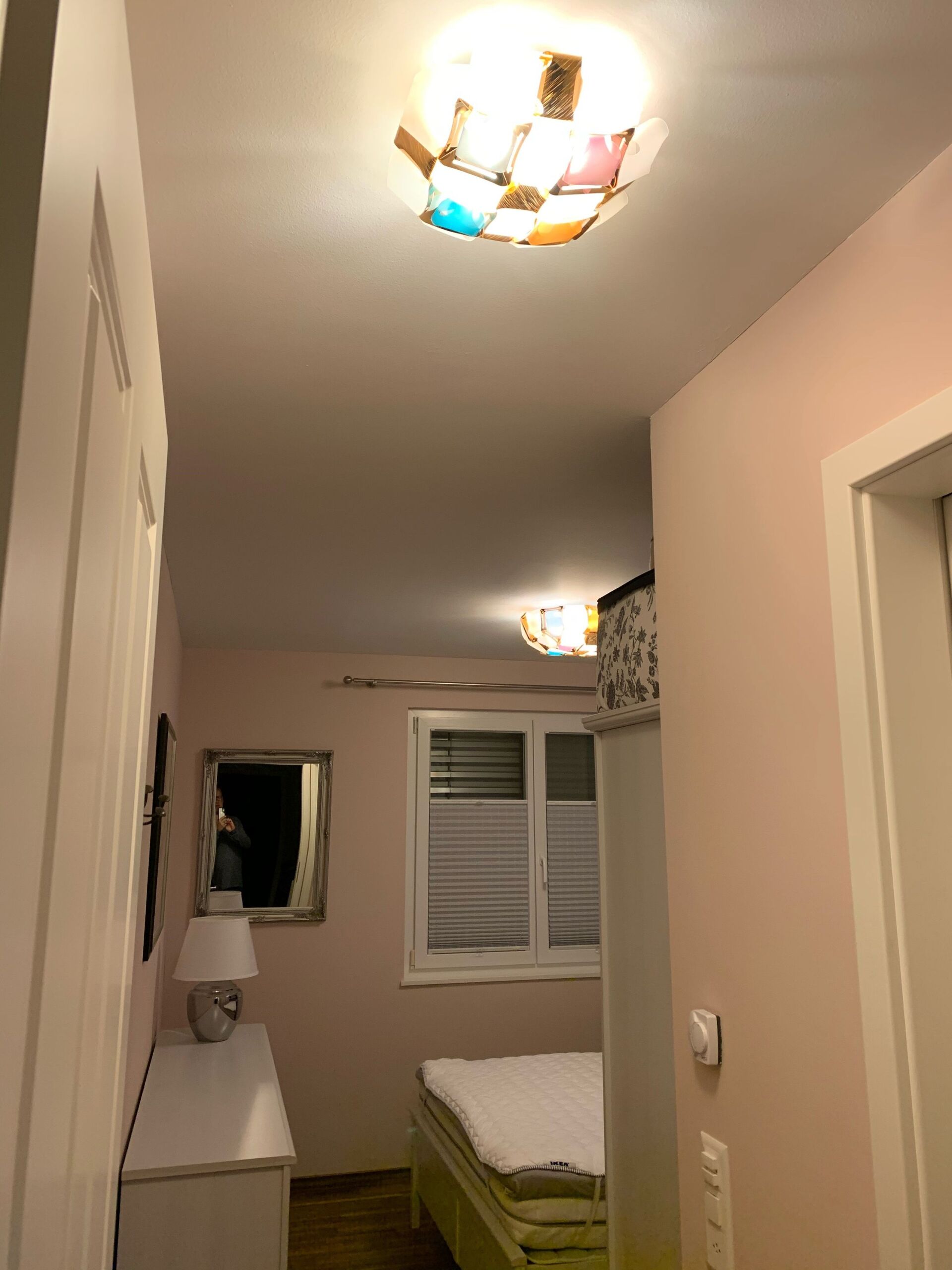 Ein Schlafzimmer mit Bett, Kommode, Lampe und Deckenleuchte.