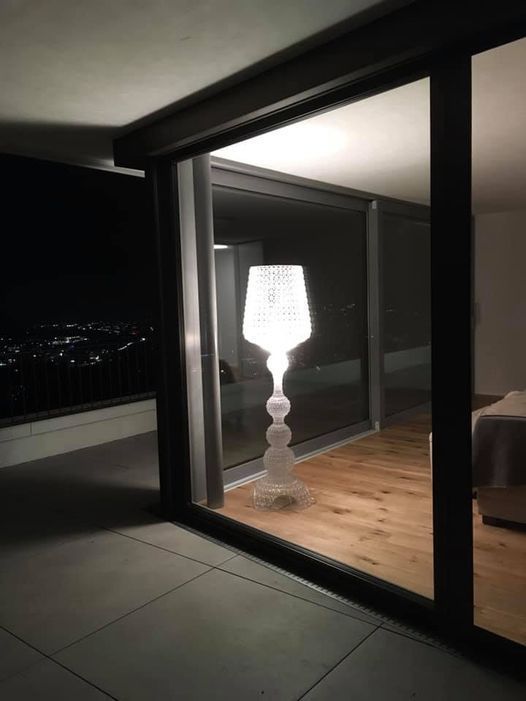 In einem dunklen Raum steht eine Lampe vor einem Fenster.