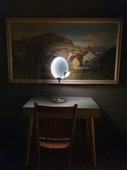 Ein Schreibtisch mit einer Lampe und einem Stuhl unter einem Gemälde.