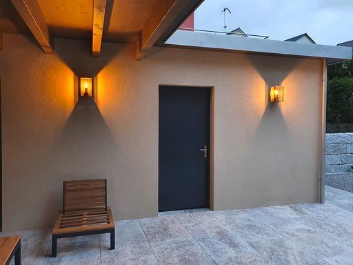 Vor einem Gebäude steht ein Stuhl mit zwei Lichtern an der Wand.