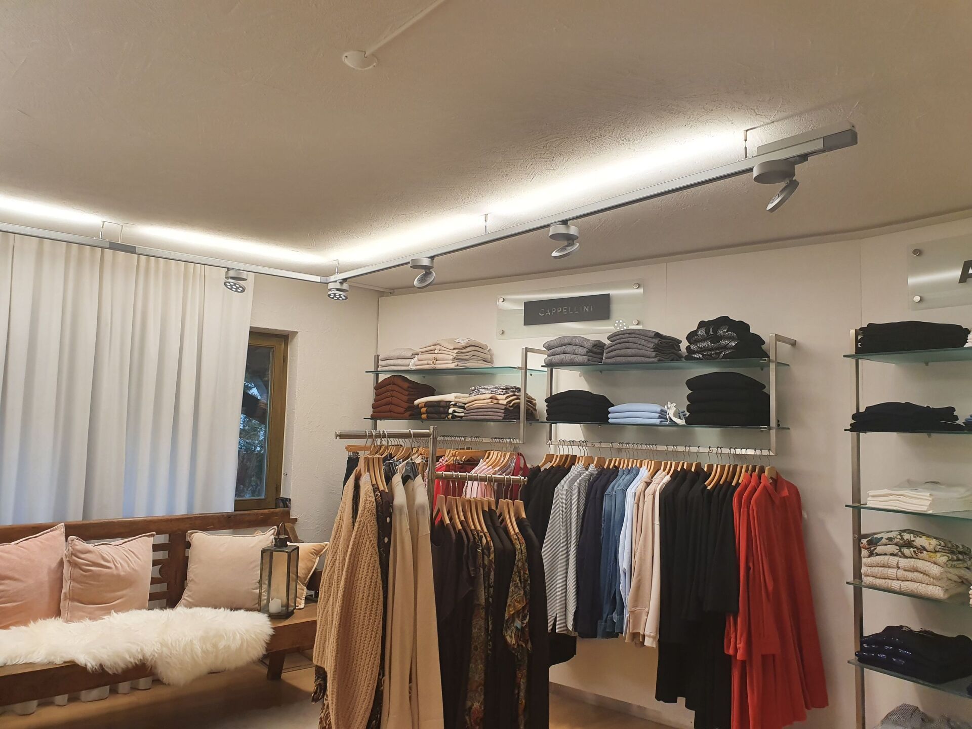 Ein Wohnzimmer mit einer Couch und an Kleiderständern hängender Kleidung.