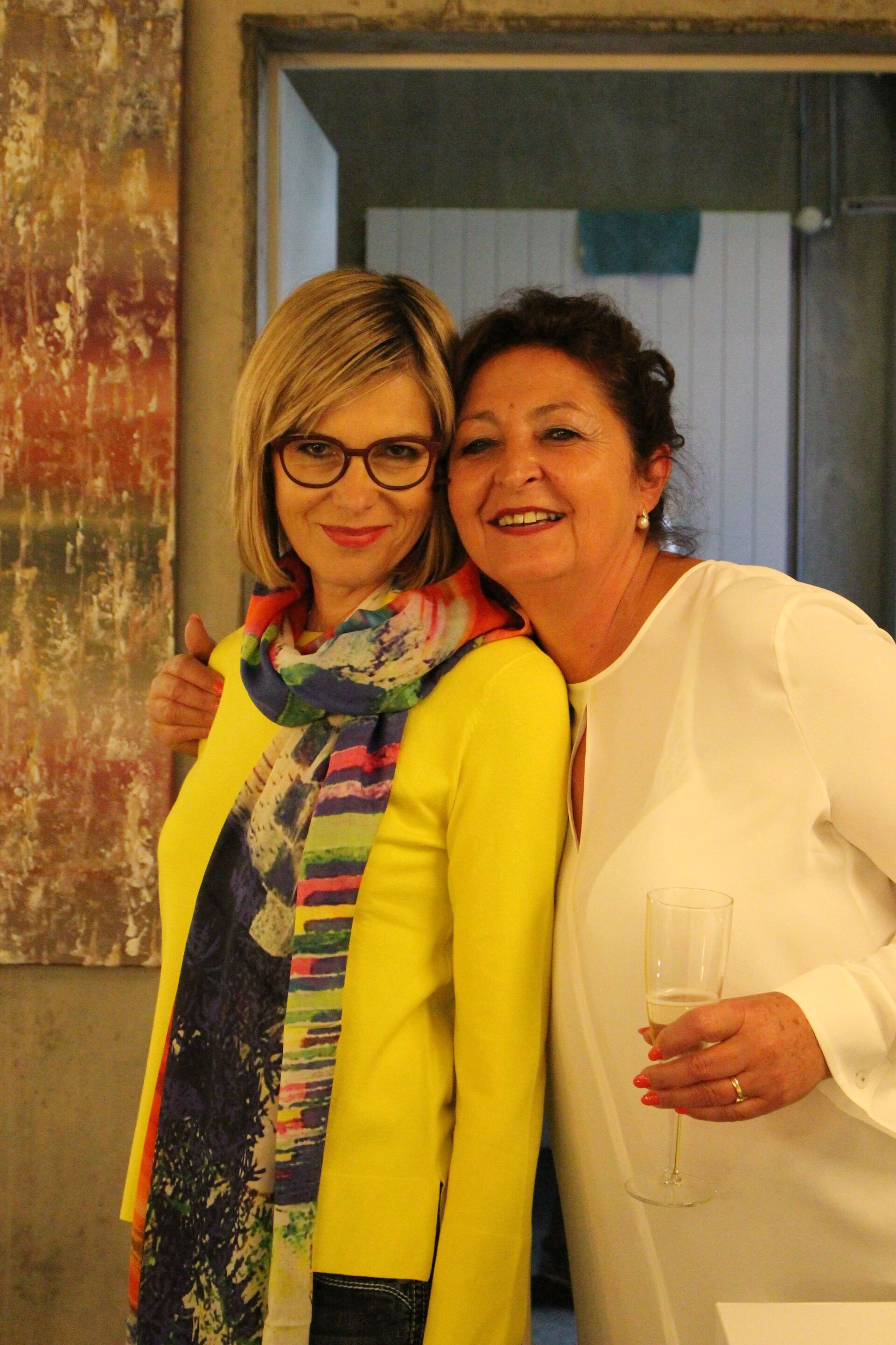 Zwei Frauen posieren für ein Foto und eine hält ein Glas Wein.