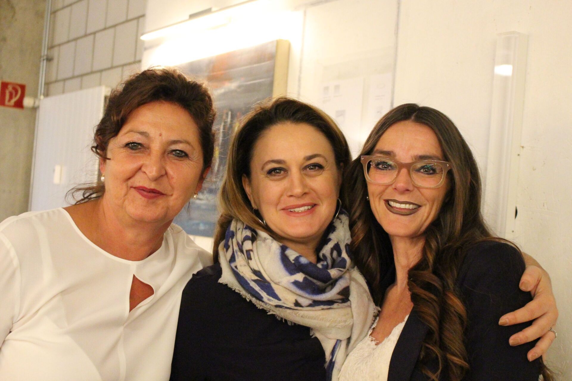 Drei Frauen posieren zusammen für ein Foto und lächeln.