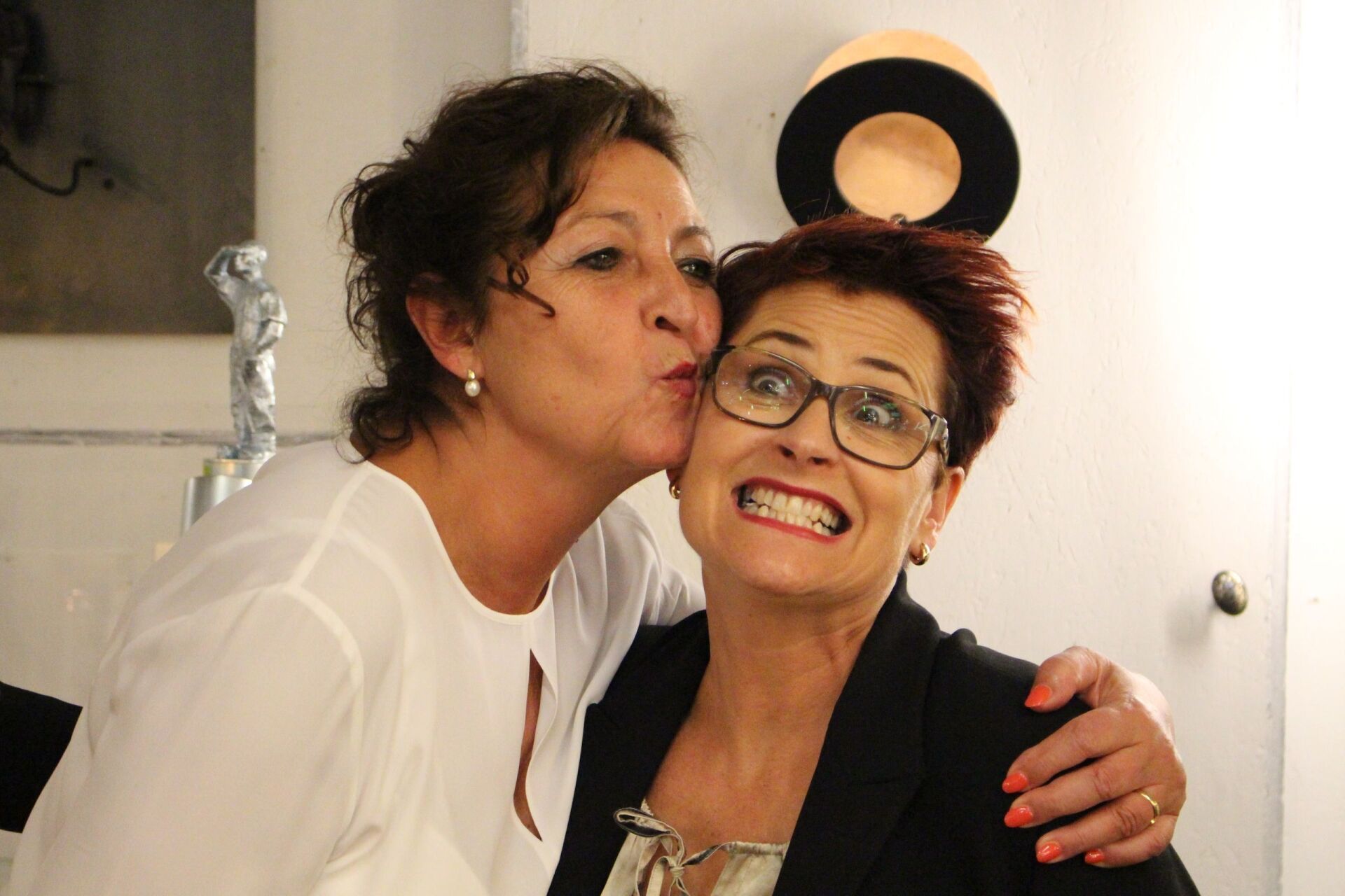 Zwei Frauen posieren für ein Foto und eine küsst die andere auf die Wange.