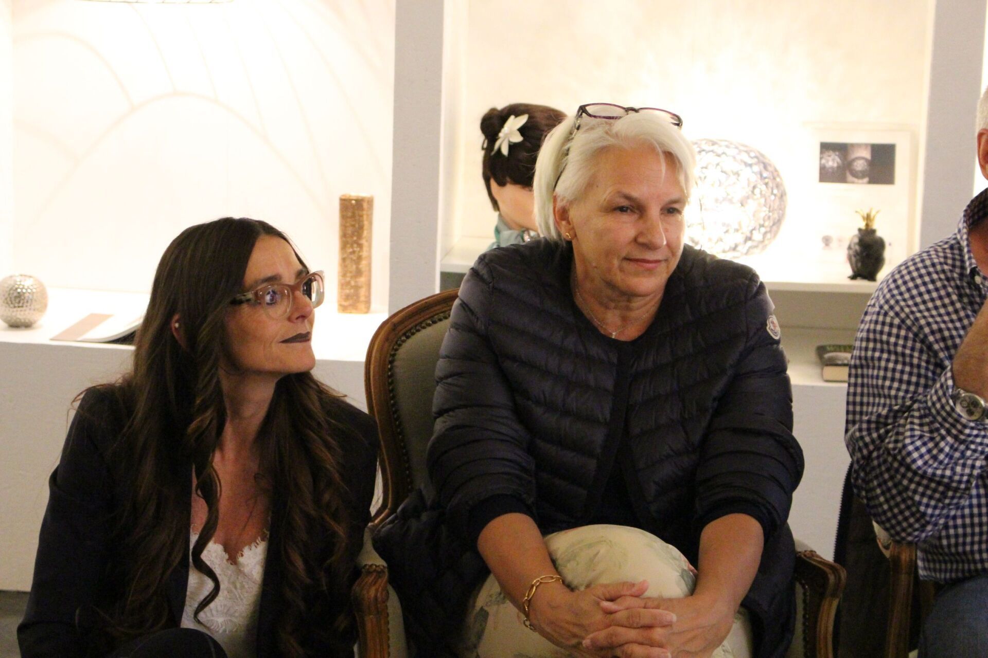 Zwei Frauen sitzen nebeneinander auf Stühlen in einem Raum.