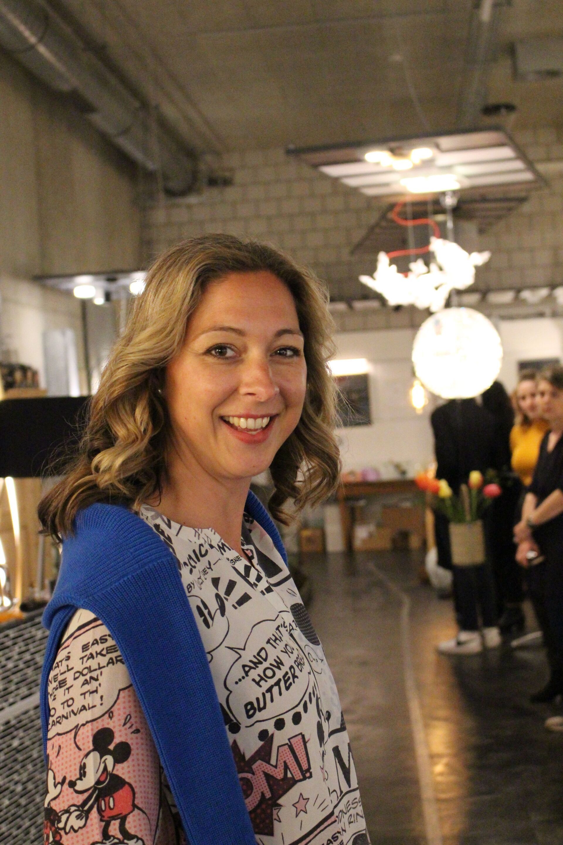 Eine Frau in einem Mickey-Mouse-Shirt lächelt in einem Raum.