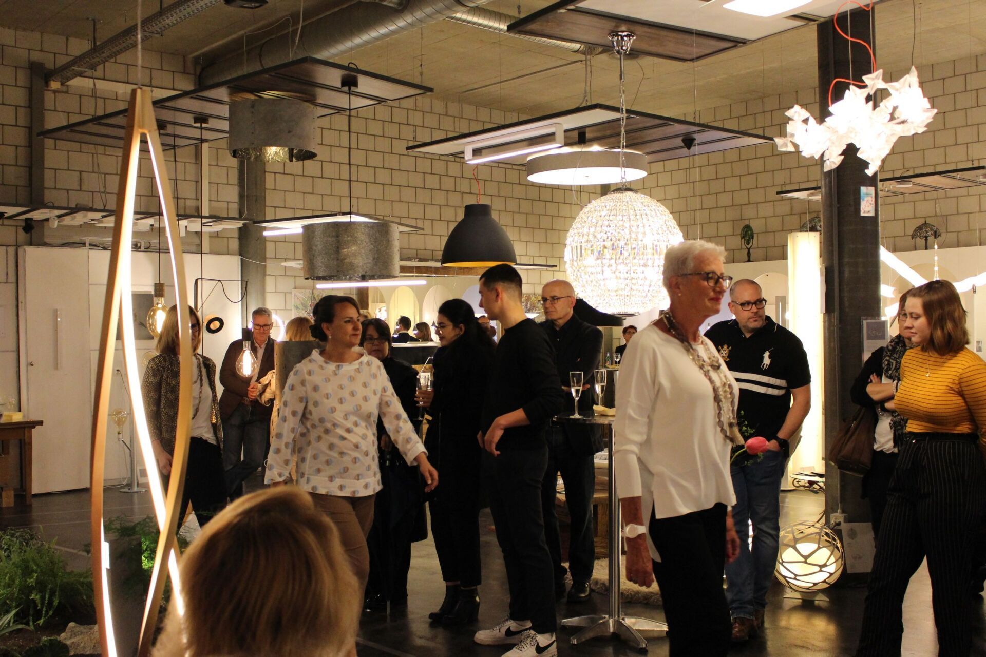 Eine Gruppe von Leuten steht in einem Raum, von dessen Decke viele Lichter hängen.