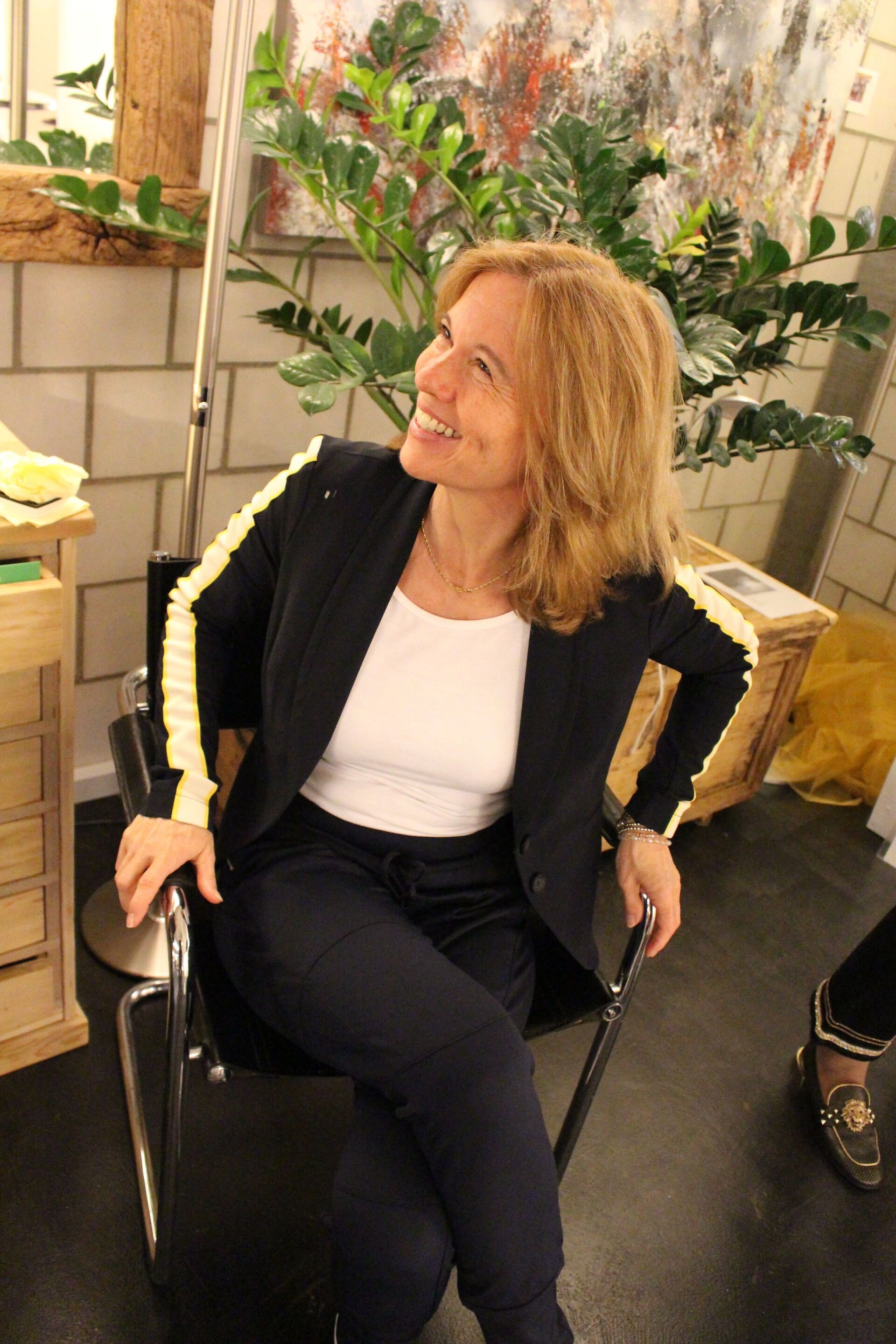 Eine Frau im Anzug sitzt auf einem Stuhl und lächelt.