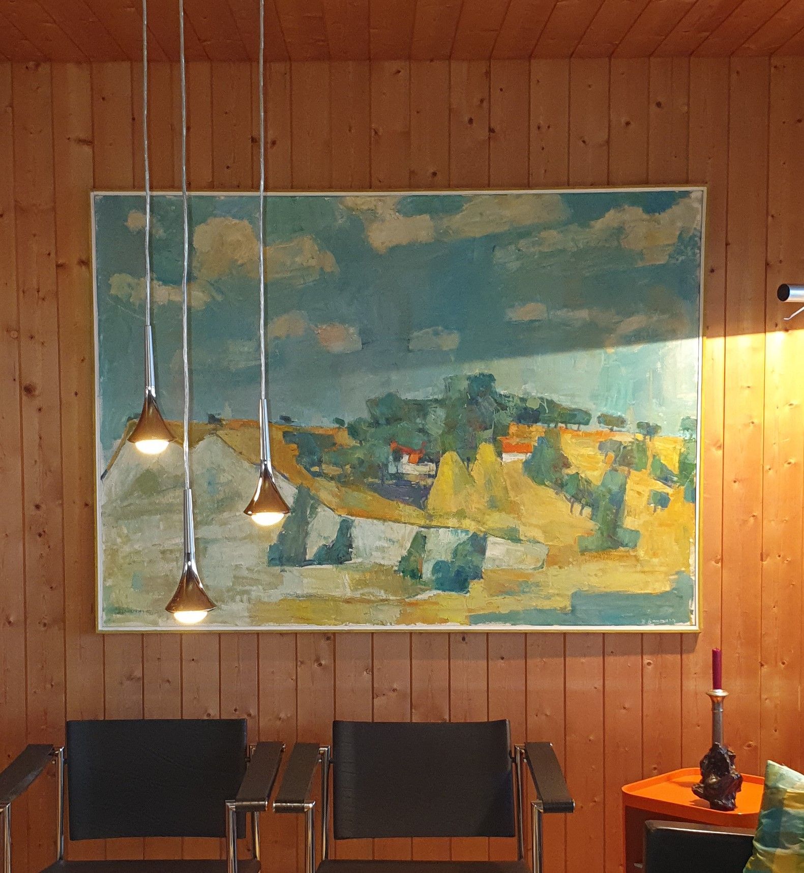 Ein großes Gemälde hängt an einer Holzwand über zwei Stühlen