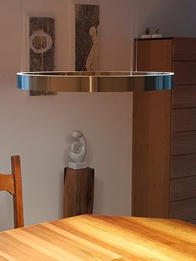 Ein Holztisch mit einer Pendelleuchte aus Edelstahl, die in einem Esszimmer von der Decke hängt.