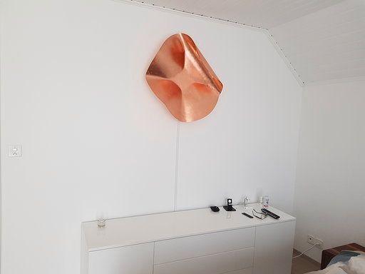 Eine Kupferskulptur hängt an einer weißen Wand in einem Wohnzimmer.