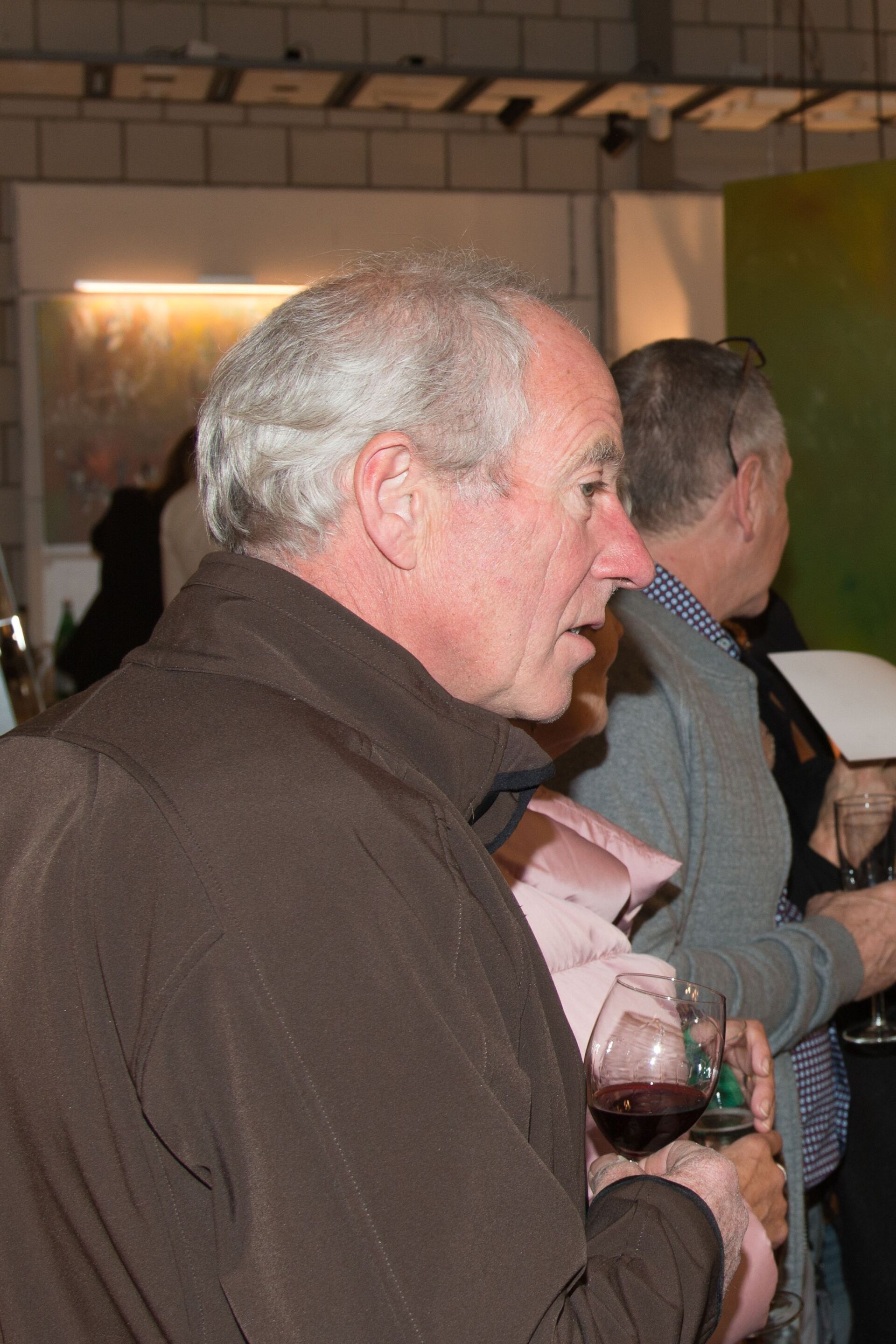 Ein Mann in einer braunen Jacke hält ein Glas Wein.