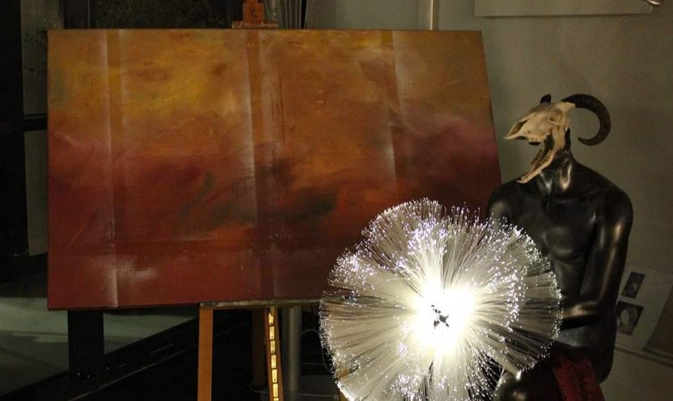 Eine Ziegenstatue steht neben einem Gemälde auf einer Staffelei.