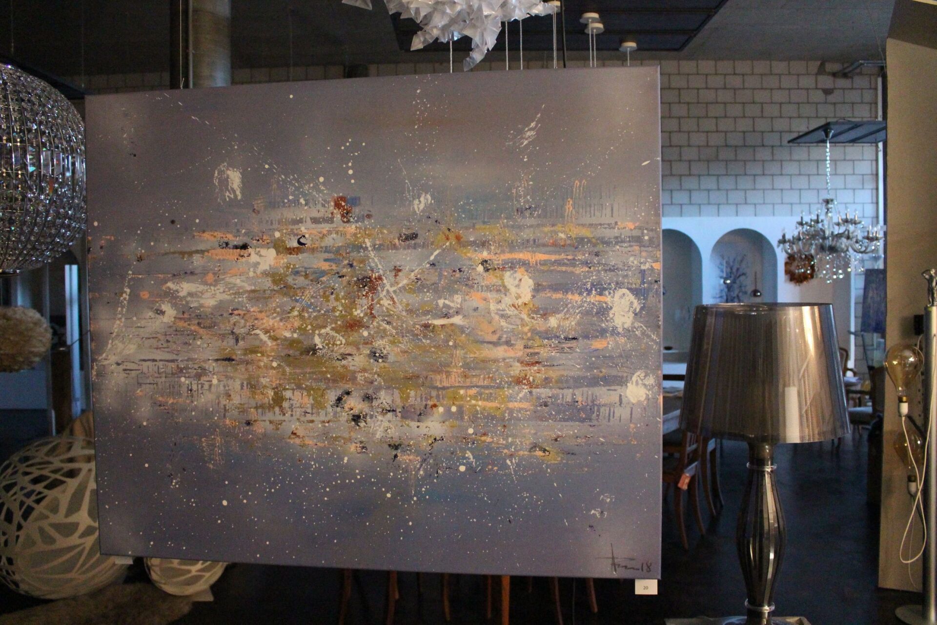 Ein großes Gemälde hängt neben einer Lampe an einer Wand.