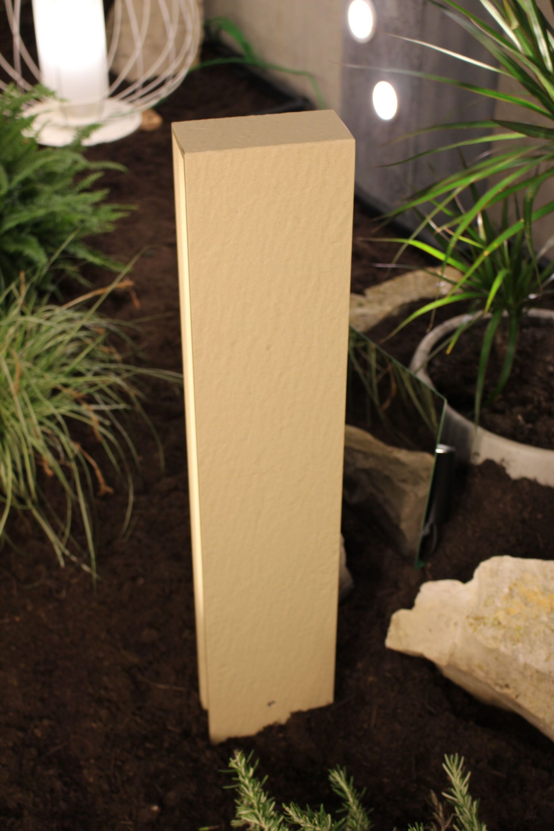 Ein Holzbuchstabe „i“ liegt im Dreck, umgeben von Pflanzen