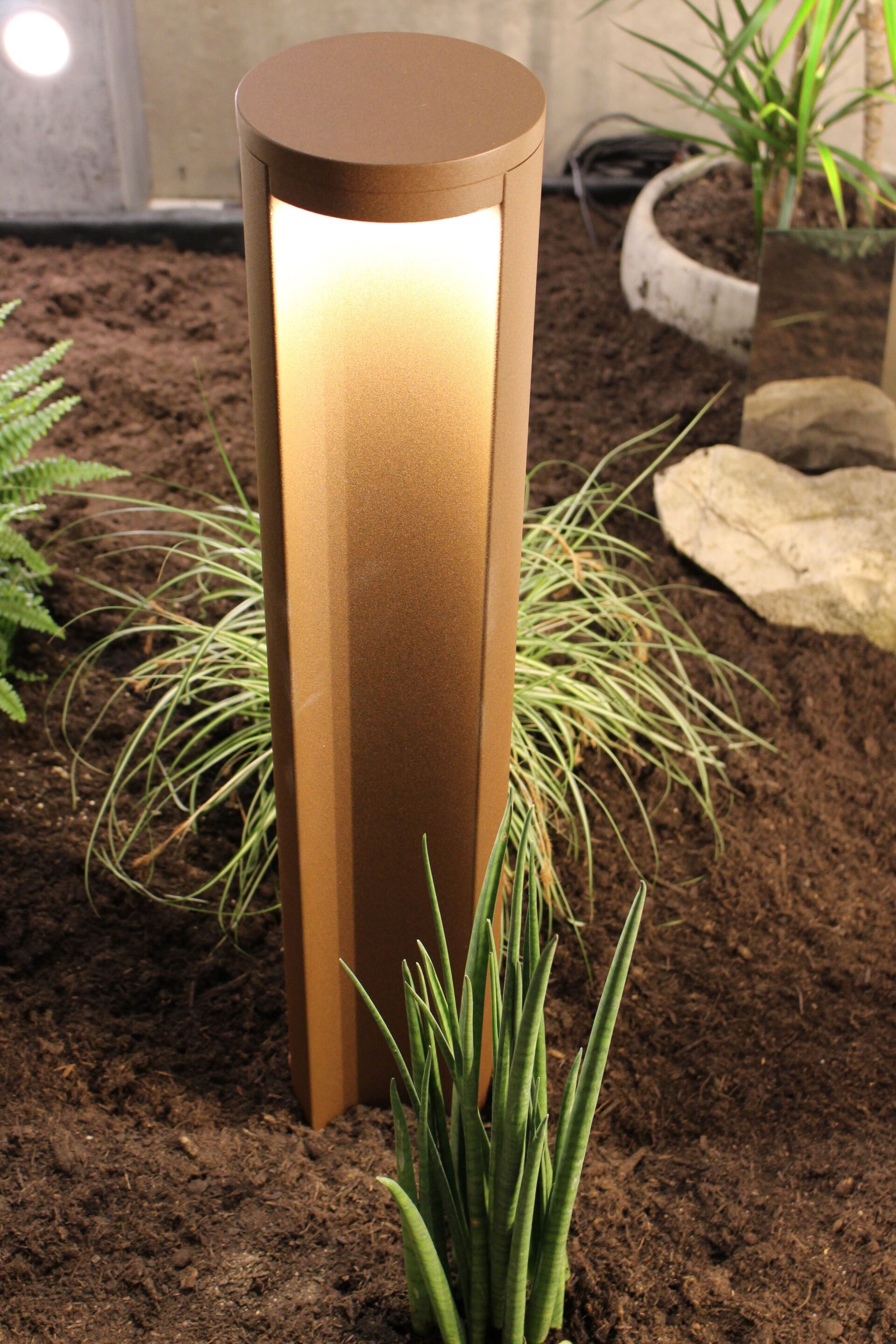 Ein brauner Pfosten mit einer Lampe darin ist von Pflanzen und Felsen umgeben.