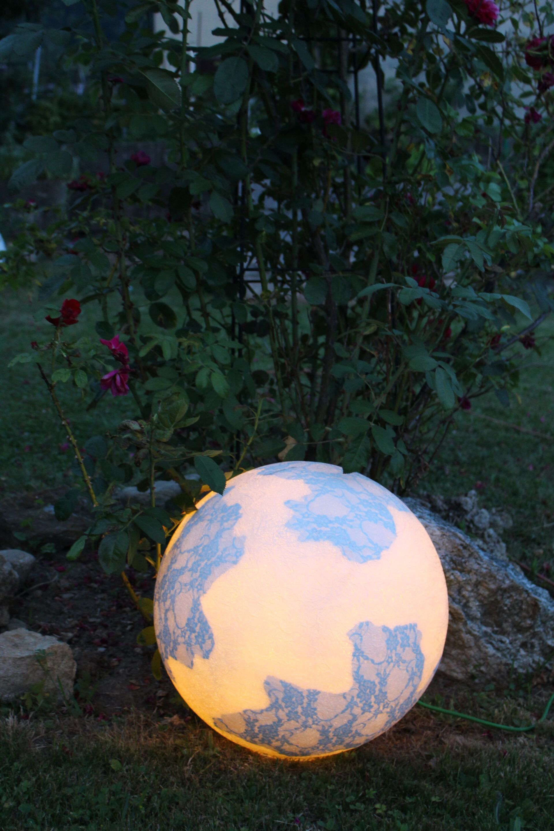 Ein Globus mit einem Licht darin steht im Gras neben einem Busch.