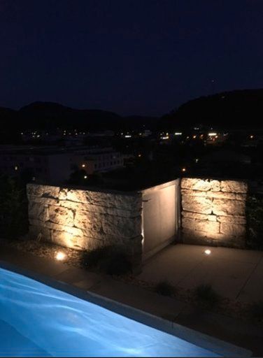 Ein Swimmingpool ist nachts beleuchtet, mit Bergen im Hintergrund