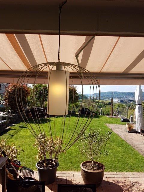 Eine Lampe, die von der Decke hängt, in einem Garten mit Topfpflanzen