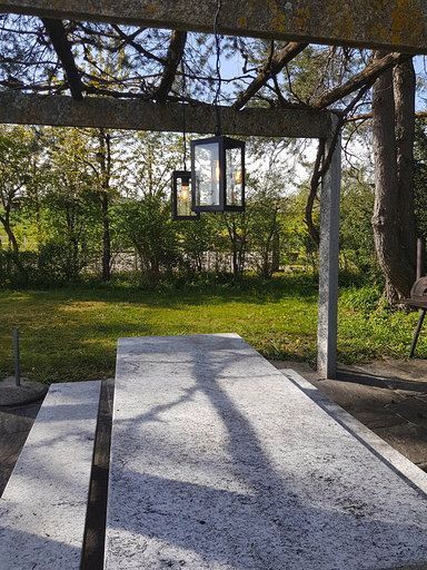 Ein Tisch und Bänke unter einer Pergola, an der eine Laterne hängt.