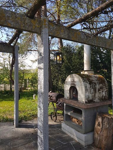 Ein Pizzaofen steht unter einer Pergola in einem Garten.