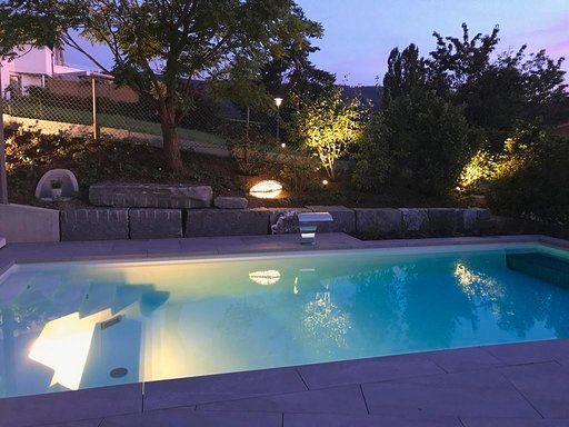 In einem Hinterhof ist ein großer Swimmingpool nachts beleuchtet.