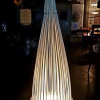 Eine Lampe aus Holzstäben steht auf einem Holzboden in einem dunklen Raum.