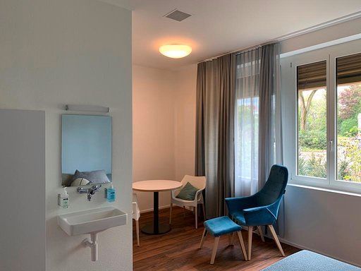 Ein Raum mit Waschbecken, Stuhl, Tisch und Fenster.