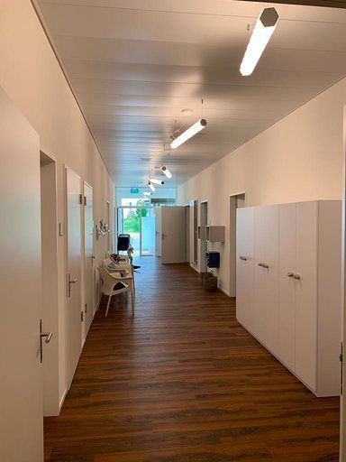 Ein langer Flur mit Holzboden und weißen Wänden in einem Krankenhaus.