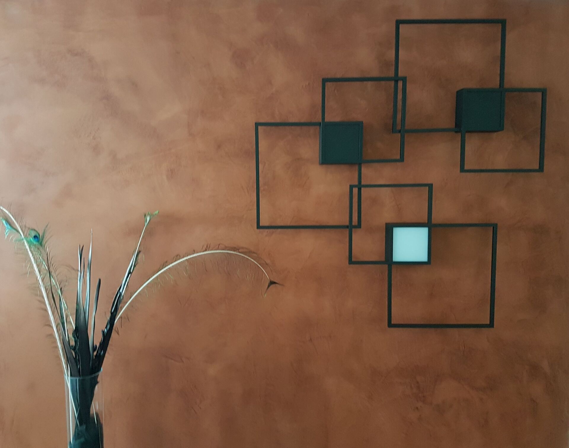 Eine Vase mit Blumen steht vor einer braunen Wand mit Quadraten darauf.