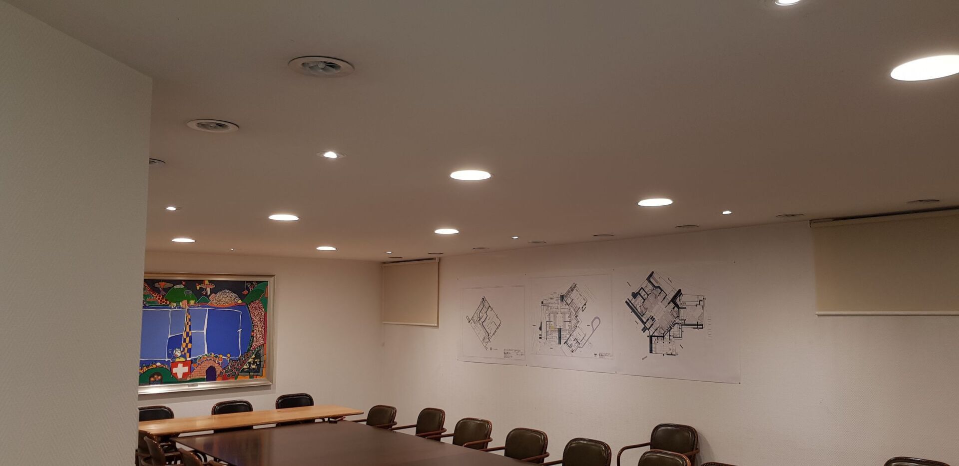 Ein Konferenzraum mit einem langen Tisch und Stühlen und einem Gemälde an der Wand.