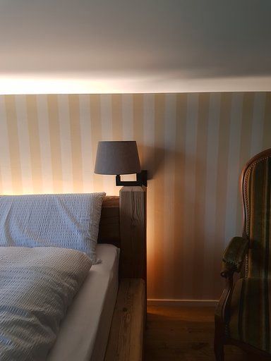 Ein Schlafzimmer mit Bett, Stuhl, Lampe und gestreifter Tapete.