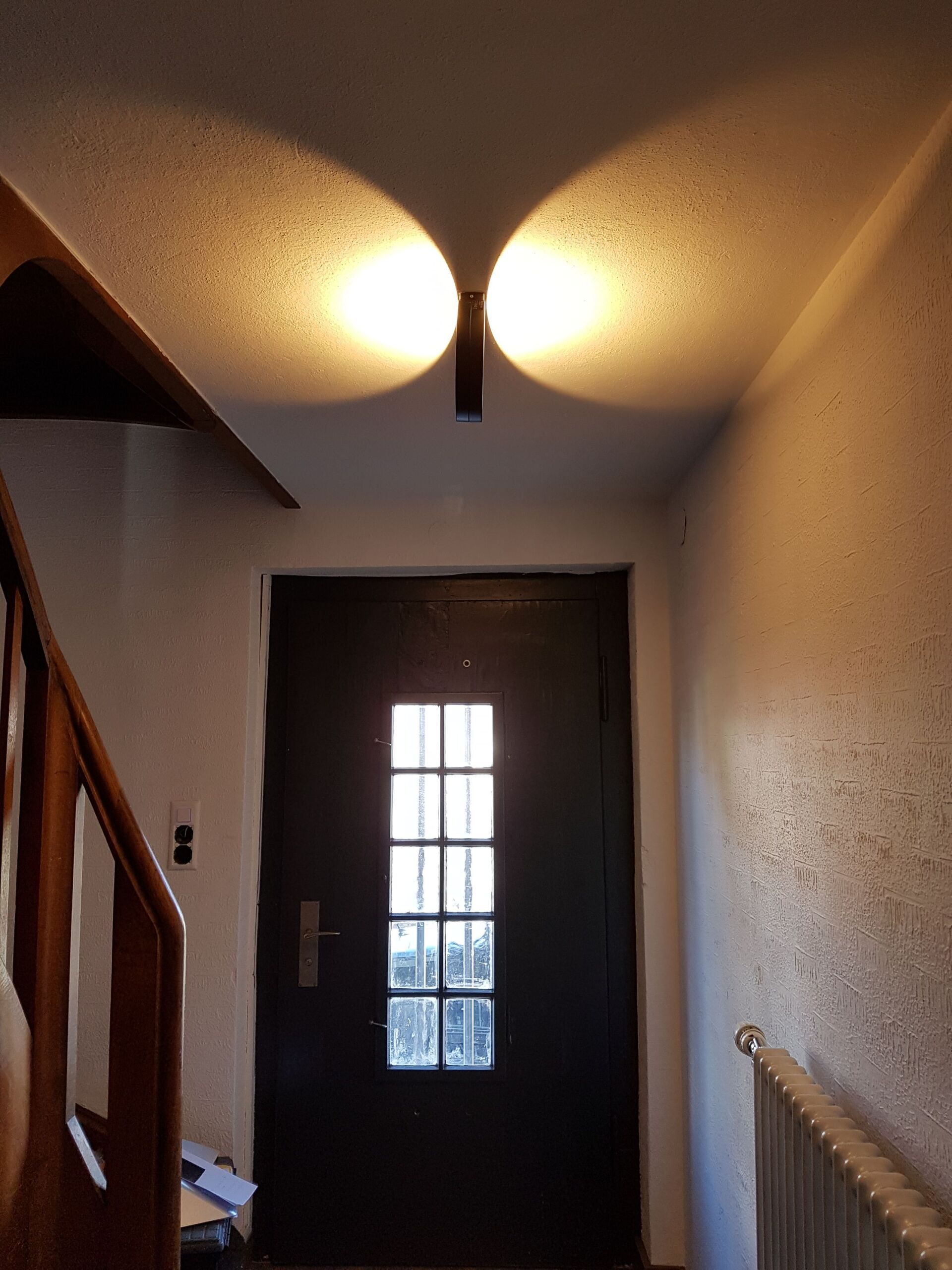 Ein Flur mit einer Holztreppe und einer schwarzen Tür.