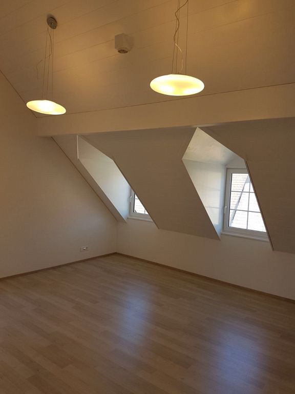 Ein leerer Raum mit Dachschräge und drei Fenstern