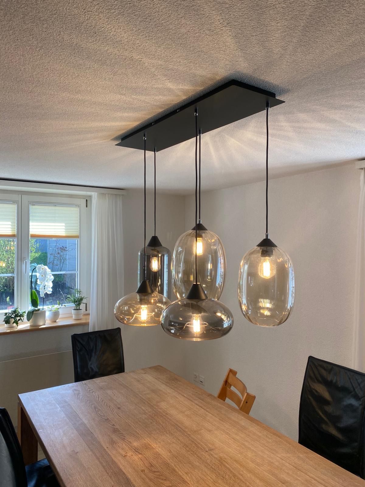 Ein Esszimmer mit einem Holztisch und Stühlen und einer Deckenleuchte, die von der Decke hängt.