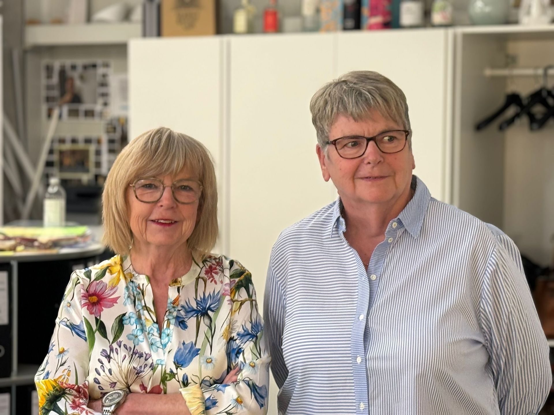 Zwei Frauen stehen mit verschränkten Armen nebeneinander in einem Raum.