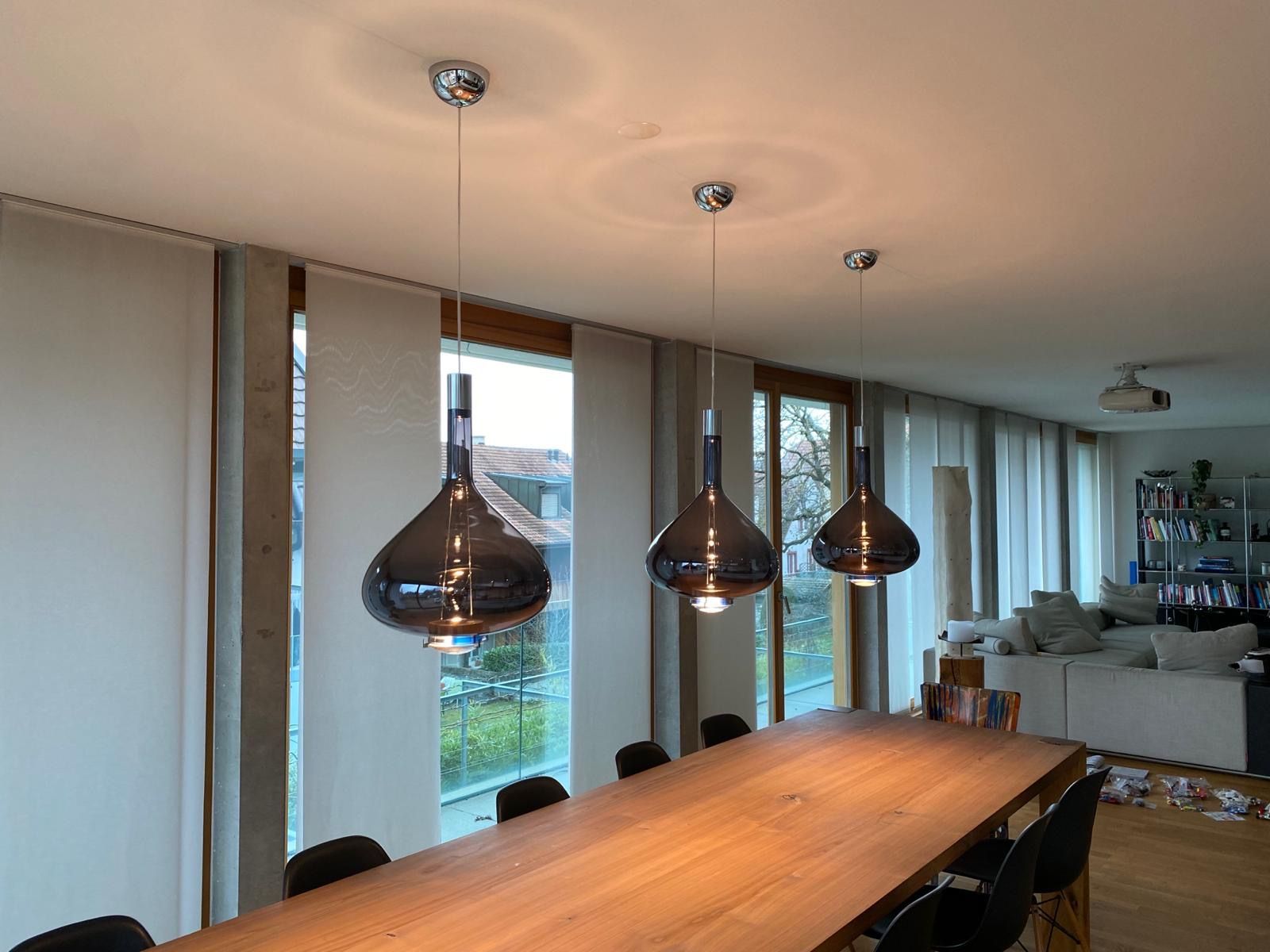 Ein Esstisch mit drei Pendelleuchten, die von der Decke hängen.