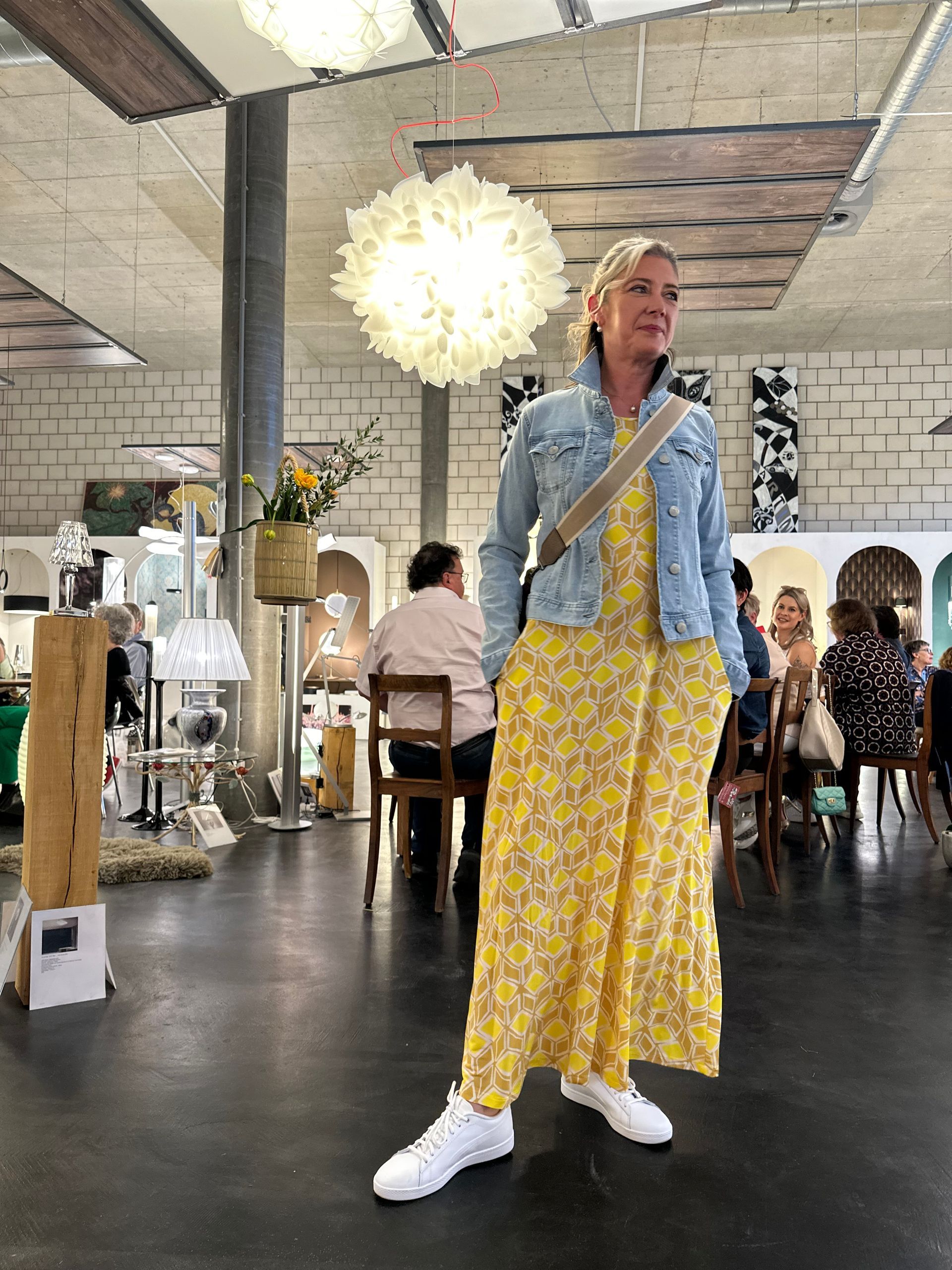 Eine Frau in einem gelben Kleid und einer Jeansjacke steht in einem Raum.