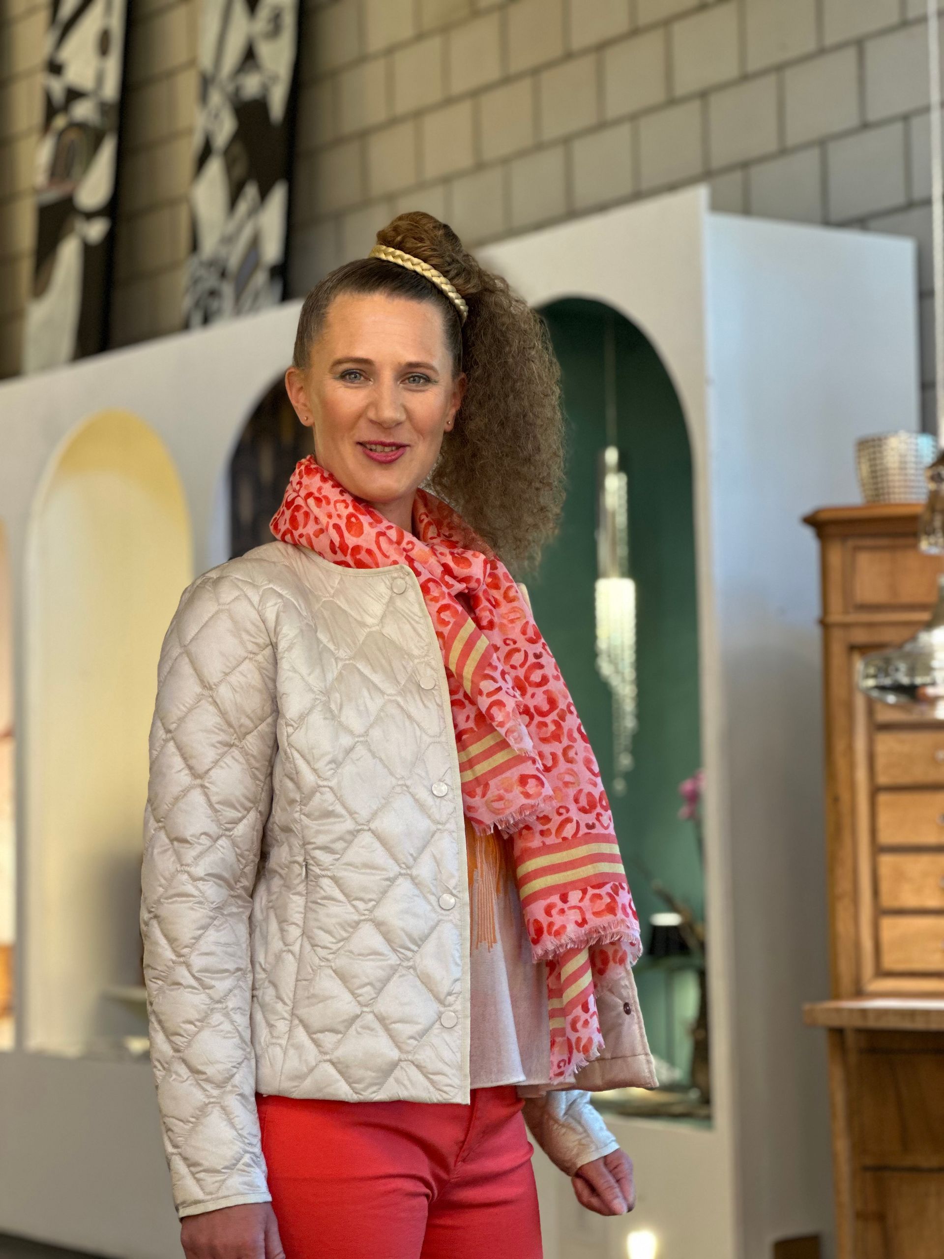 Eine Frau mit einer weißen Jacke und roten Hosen steht in einem Raum.