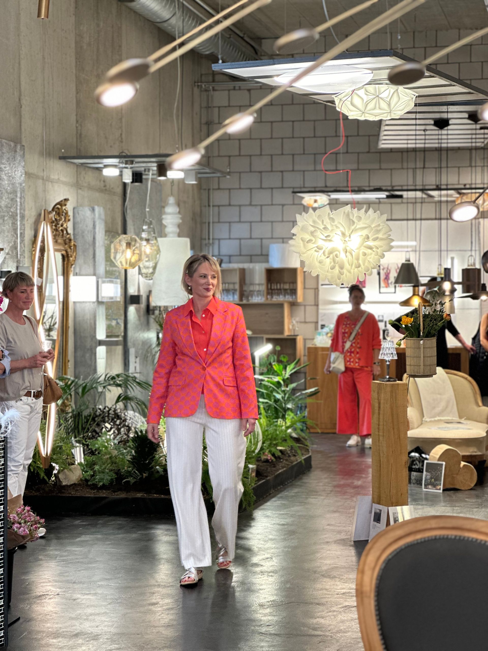 Eine Frau in einer rosa Jacke und weißen Hosen geht durch ein Geschäft.