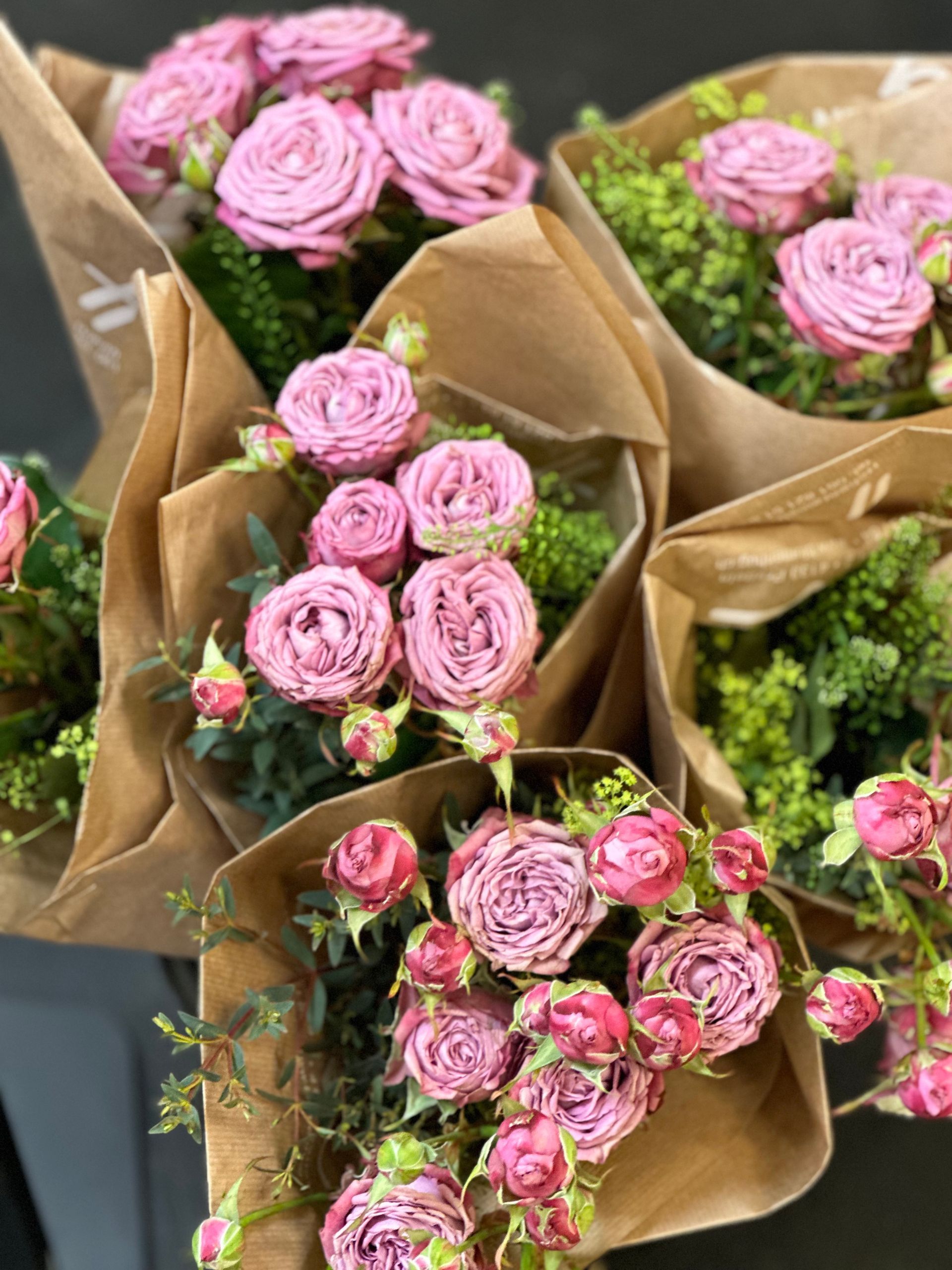 Ein Strauß rosa Rosen, in braunes Papier eingewickelt, auf einem Tisch.