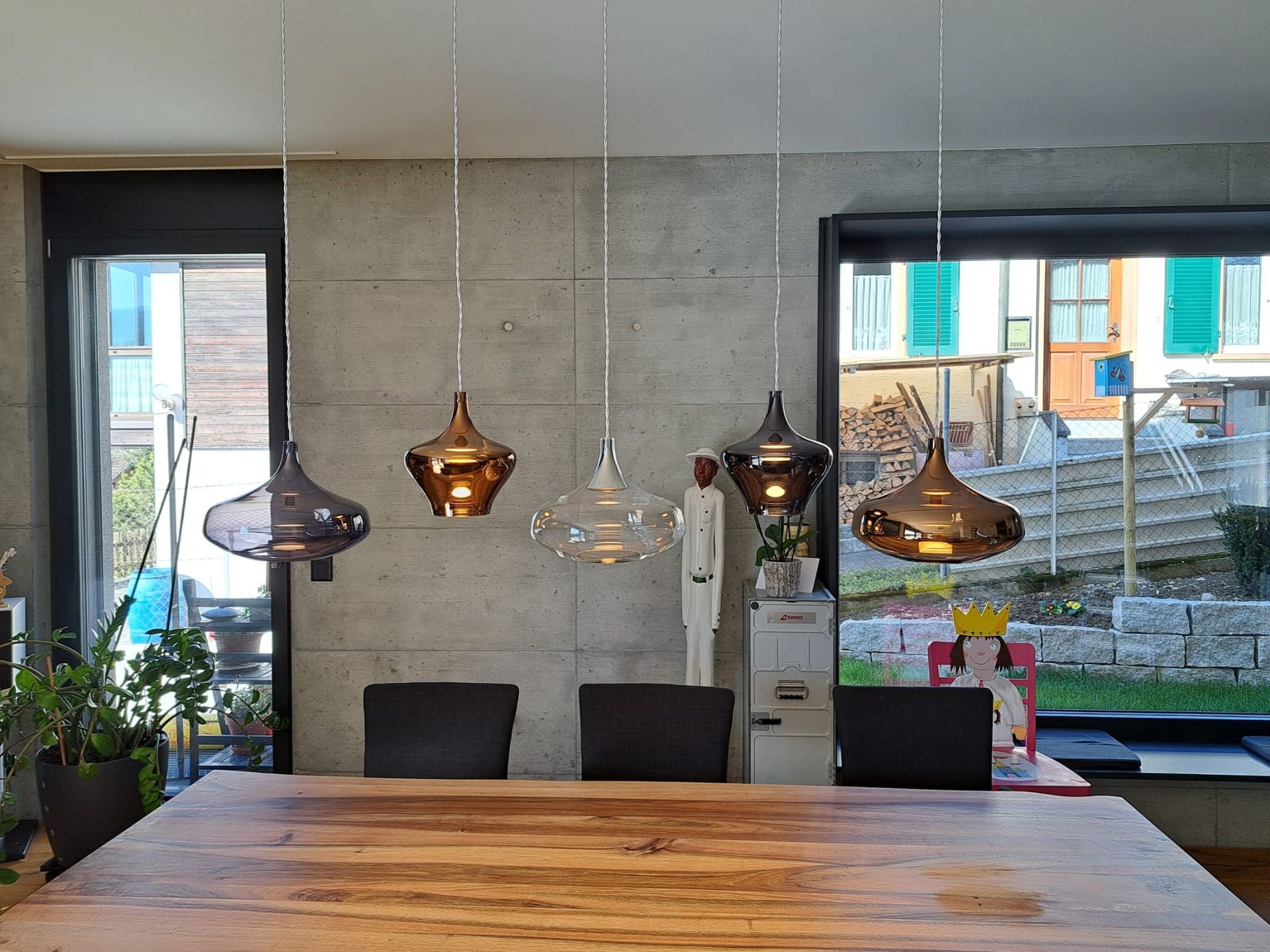 Ein Esszimmer mit einem Holztisch und Stühlen und Pendelleuchten, die von der Decke hängen