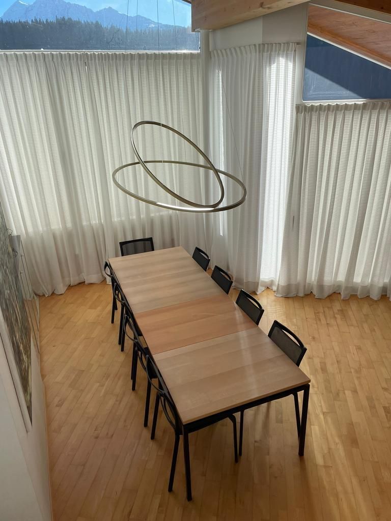 Ein langer Holztisch und Stühle in einem Raum mit weißen Vorhängen.